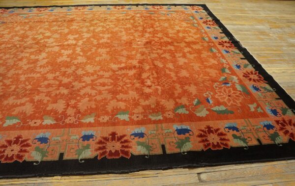 Low-pile orange rug with scrolling florals and a dark border accented by blue, red, and green motifs.