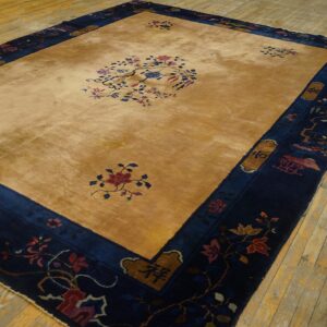 Gold and navy rug with floral patterns centered on distressed light wooden plank flooring.