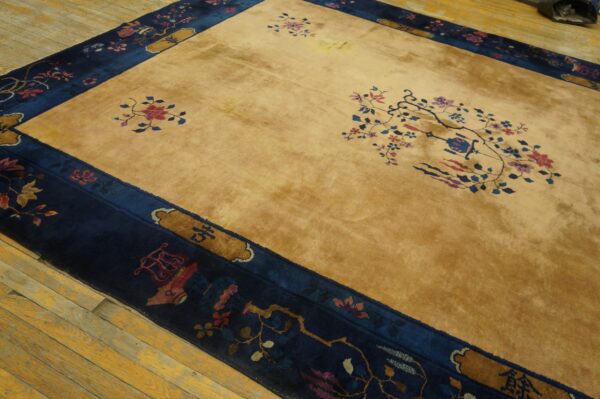 Gold high-pile rug with a wide navy border and stylized red and blue florals on distressed wood flooring.