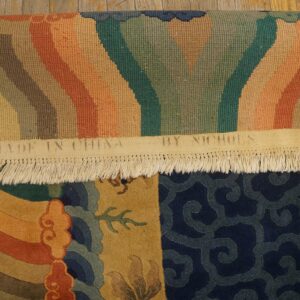 A colorful rolled rug displays gold, navy, orange, and green patterns, resting on light brown distressed wood planks.