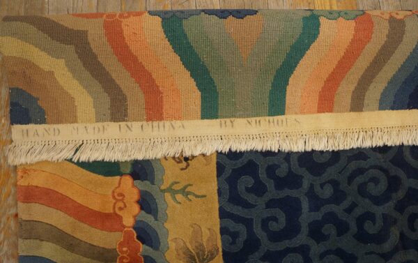 A colorful rolled rug displays gold, navy, orange, and green patterns, resting on light brown distressed wood planks.