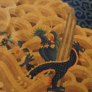Close-up of a carved rug pattern showing a blue dragon and flowers against ochre-colored waves.