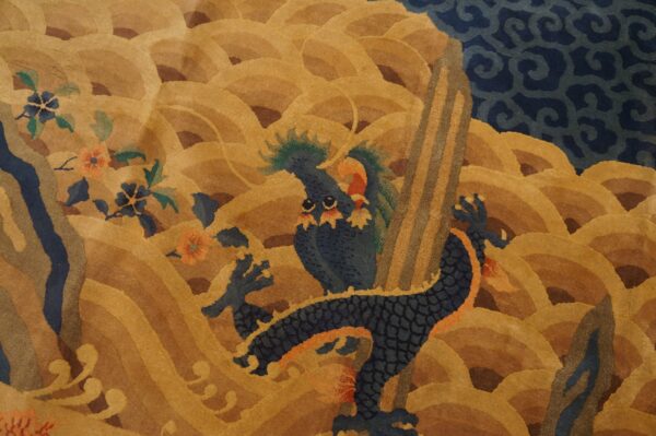 Close-up of a carved rug pattern showing a blue dragon and flowers against ochre-colored waves.