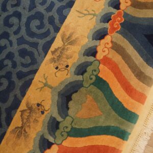 Colorful rug detail featuring dark blue scrolls, stylized gold figures, and thick stripes on wood flooring.