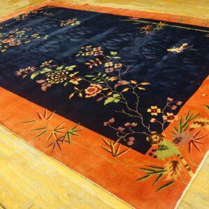 Plush navy rug with floral pattern and wide orange border lies on reflective light wood floors.
