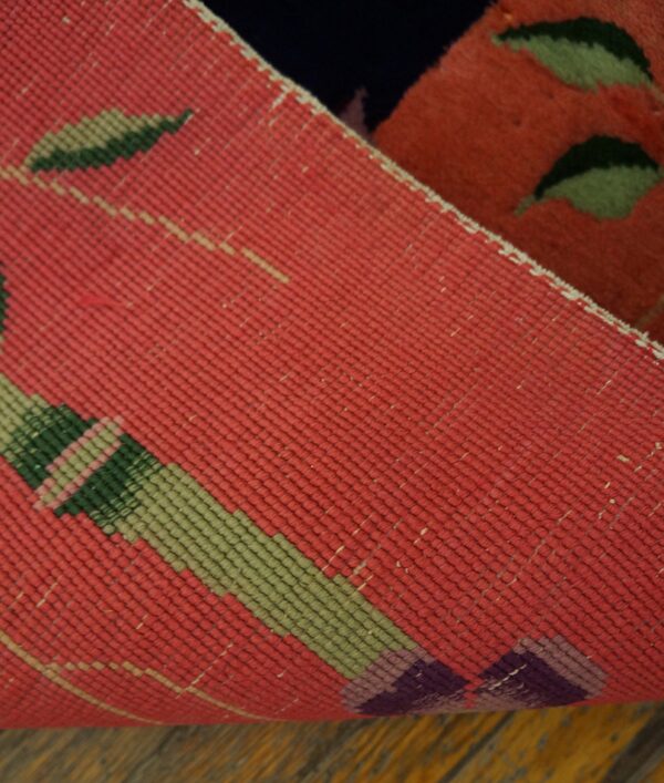 Detail of a coral and green patterned rug backing folded to show the plush pile face on dark wood flooring.