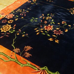 Navy rug with a bright orange border and detailed floral pattern on worn yellow wooden floors.