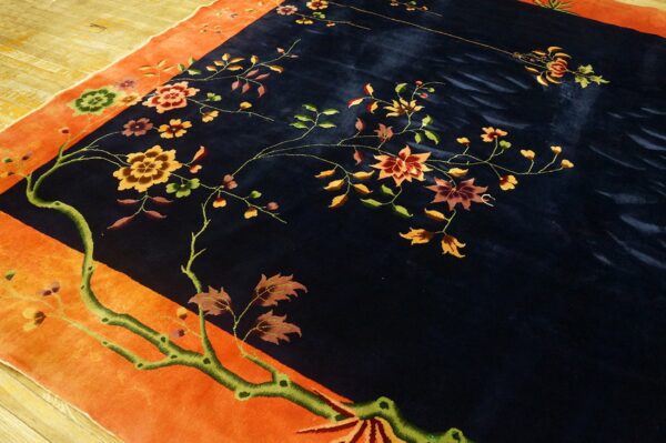 Navy rug with a bright orange border and detailed floral pattern on worn yellow wooden floors.