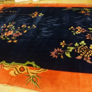 A deep navy rug with high pile and an orange-red border featuring stylized floral and bamboo motifs.