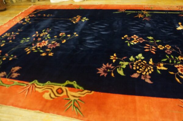 A deep navy rug with high pile and an orange-red border featuring stylized floral and bamboo motifs.