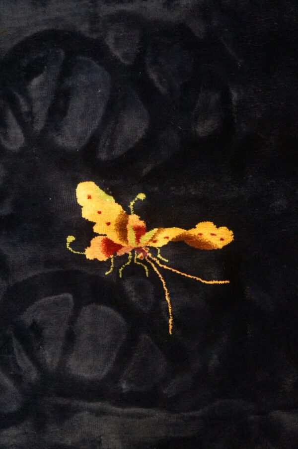 Detail view of a velvety dark rug showing a vibrant gold and maroon butterfly pattern.