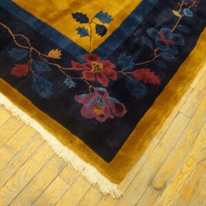 Navy and gold floral rug corner with red and purple details rests on yellow wooden plank flooring.
