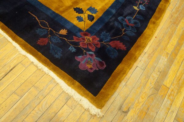 Navy and gold floral rug corner with red and purple details rests on yellow wooden plank flooring.