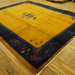 Mustard yellow rug with a navy floral border and center motif laying on worn wooden floors.