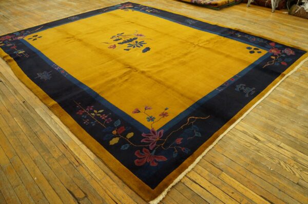 Mustard yellow rug with a navy floral border and center motif laying on worn wooden floors.