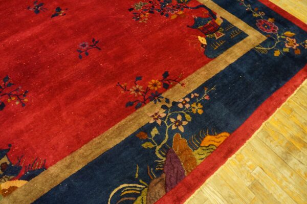 Red field rug with blue border featuring floral and pagoda patterns rests on light wood planks.