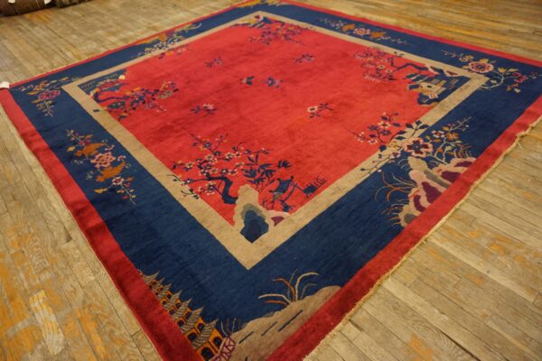 Ornate red rug featuring blue landscape borders and tan geometric framing on worn light brown wood planks.