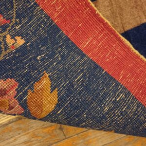 The tightly woven underside of a blue and red rug with geometric florals rests on distressed wood flooring.