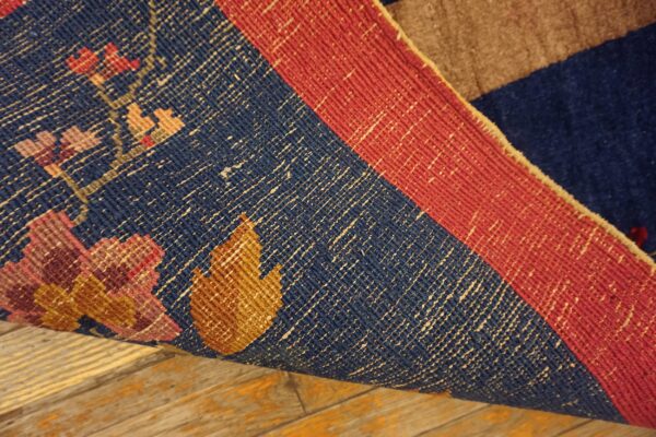 The tightly woven underside of a blue and red rug with geometric florals rests on distressed wood flooring.