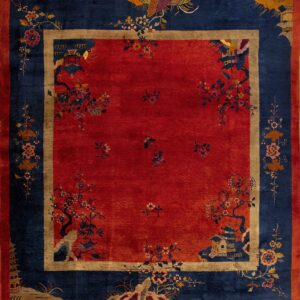 Red square rug with a navy blue border and elaborate multicolor flowering tree and pagoda designs.