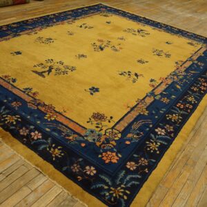Square yellow rug with a navy floral border and delicate scattered patterns rests on distressed wooden flooring.