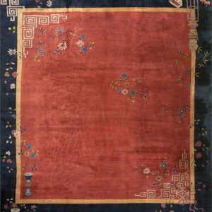 Rust red rug with a dark blue border decorated with floral vines, symbols, and geometric fret motifs.