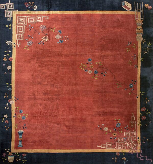 Rust red rug with a dark blue border decorated with floral vines, symbols, and geometric fret motifs.