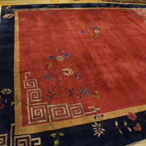 Large red rug featuring scattered florals, gold trim, and a wide navy blue border on wooden planks.
