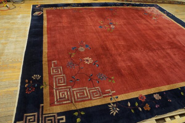 Large red rug featuring scattered florals, gold trim, and a wide navy blue border on wooden planks.