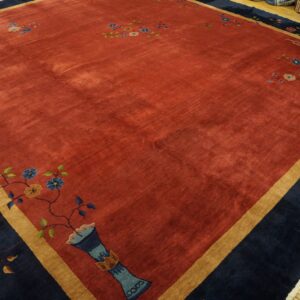 A velvety rust-toned rug with navy and tan borders displaying stylized floral and geometric patterns.