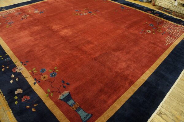 A velvety rust-toned rug with navy and tan borders displaying stylized floral and geometric patterns.
