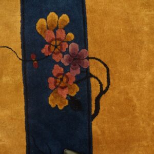 Gold rug with a navy stripe and floral pattern resting beside distressed yellow wood flooring.