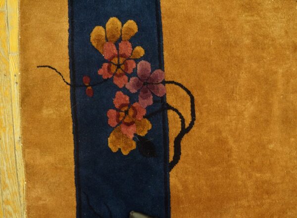 Gold rug with a navy stripe and floral pattern resting beside distressed yellow wood flooring.