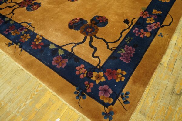 Gold rug with a navy border displays large floral patterns in rust, purple, and blue on wood planks.