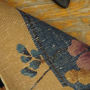 Tan rug backing and floral-patterned purple and blue pile rest on distressed yellow hardwood planks.