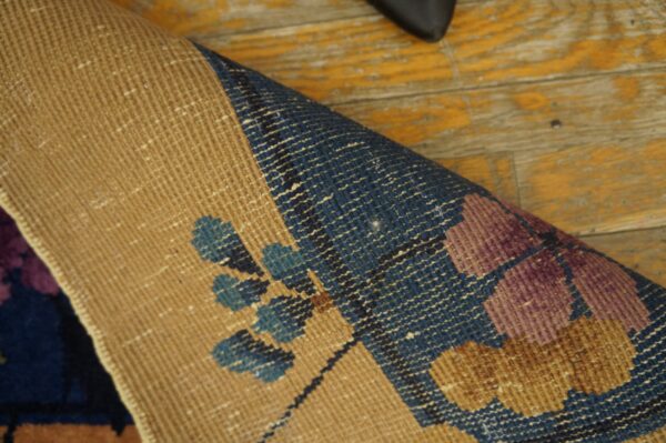 Tan rug backing and floral-patterned purple and blue pile rest on distressed yellow hardwood planks.