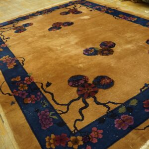 Gold field rug with a deep blue border featuring stylized red and pink floral designs on wooden planks.