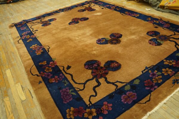 Gold field rug with a deep blue border featuring stylized red and pink floral designs on wooden planks.