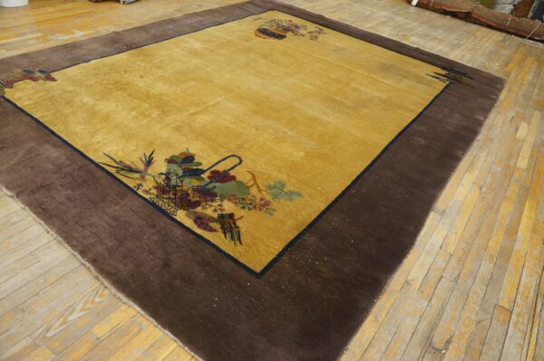 Golden-yellow rug with a dark brown border and colorful corner floral designs on plank wood floor.