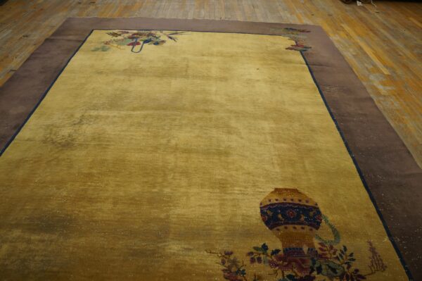 Yellow gold rug featuring stylized vase motifs and a broad brown border on rustic wood flooring.