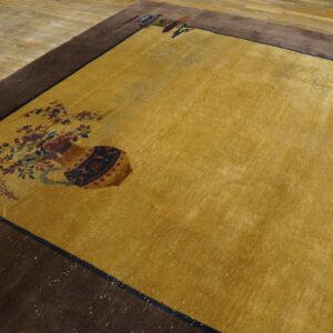 Low-pile yellow rug with a wide brown border and vase and flower designs on light wood flooring.