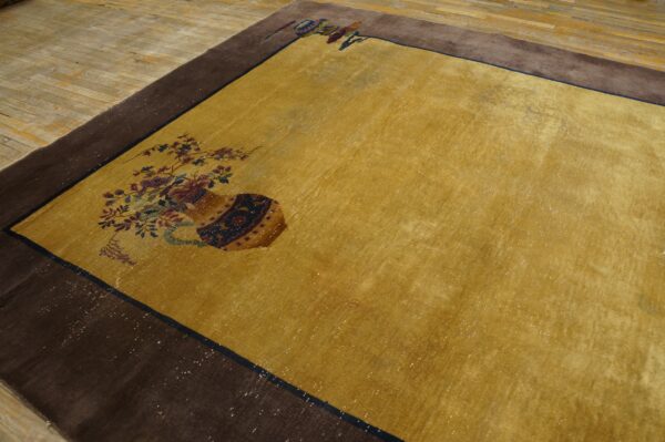 Low-pile yellow rug with a wide brown border and vase and flower designs on light wood flooring.