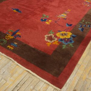 Red rug with stylized multi-colored florals and brown border rests on distressed wood flooring.