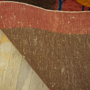Close-up showing the red and brown woven rug backing curled onto yellow distressed wooden floorboards.
