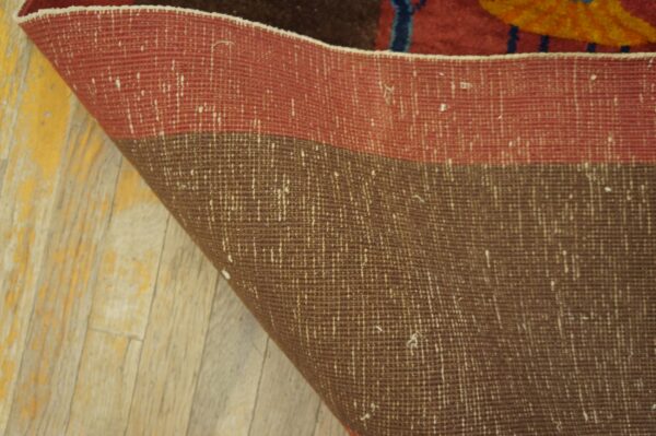 Close-up showing the red and brown woven rug backing curled onto yellow distressed wooden floorboards.