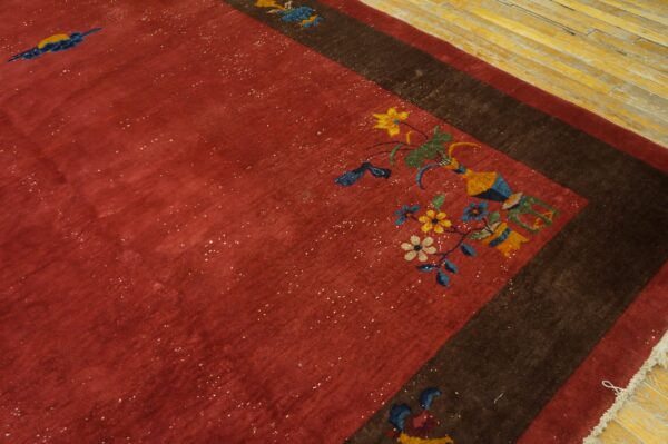 Rust-colored rug with colorful floral vase motifs and a dark border stripe over yellow hardwood floor.