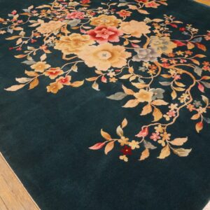 Teal low-pile rug featuring centered golden and pink floral sprays on rustic hardwood flooring.