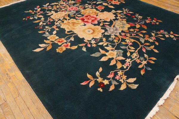 Teal low-pile rug featuring centered golden and pink floral sprays on rustic hardwood flooring.