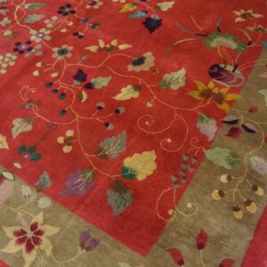 Red field rug featuring colorful scattered flowers and vines, bordered in taupe, resting on wood planks.