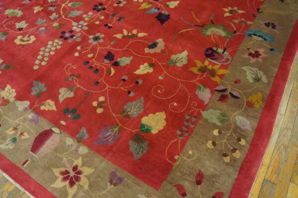 Red field rug featuring colorful scattered flowers and vines, bordered in taupe, resting on wood planks.